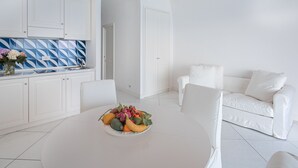 Ein modernes, weißes Wohnzimmer mit einem Essbereich, gedecktem Tisch, einem weißen Sofa und einer Küche mit weißen Schränken und einer blau gemusterten Spritzschutzleiste.