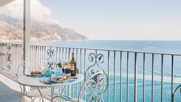 Ein Balkon mit Esstisch, der auf eine Küstenlandschaft mit blauem Himmel und weiter Sicht auf das Land blickt.