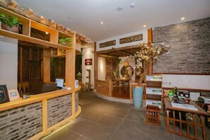 Un espace d’accueil comprenant un comptoir de réception en bois, un coin salon avec des chaises et une plante décorative.