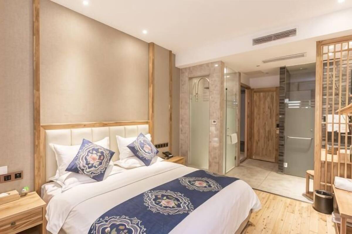 Habitación de hotel con cama, mesitas de noche, zona de ducha y un separador de madera.
