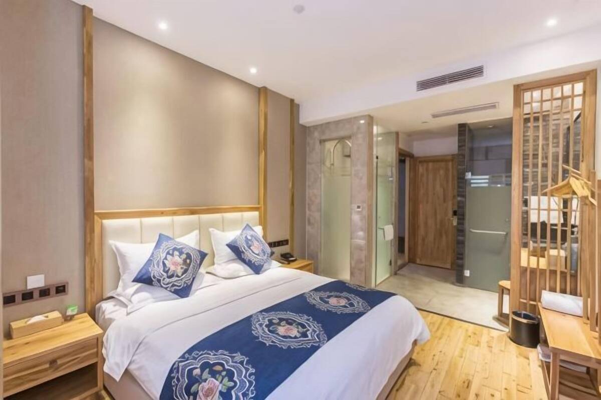 Una habitación de hotel moderna con una cama grande, una mesita de noche de madera, un escritorio y una puerta corredera que da a un baño.