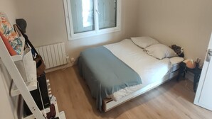 A bedroom with a bed, a window, a radiator, and a white wall. - South-facing, pleasant, quiet 65 ㎡ (Montpellier)