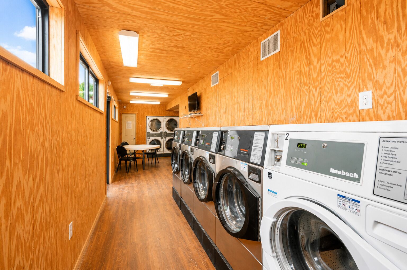 A laundry facility with multiple washing machines, wooden walls, and a table with chairs.