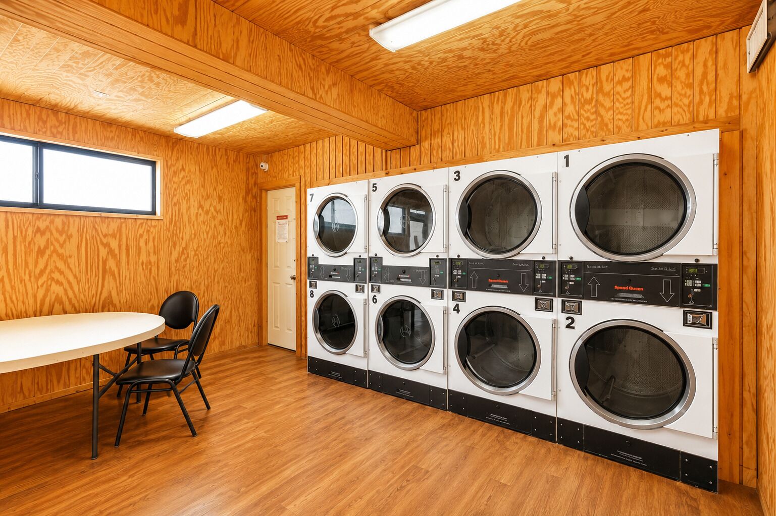 A laundry room with multiple washing machines, a table, chairs, and wooden walls.