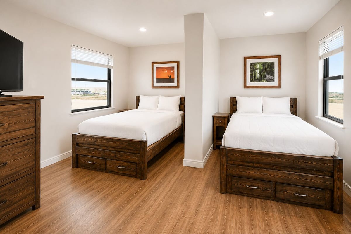 Un dormitorio con dos camas de madera, un aparador y un televisor.