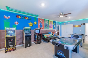 A room with arcade games, a foosball table, and a sofa with a Mario-themed pillow.
