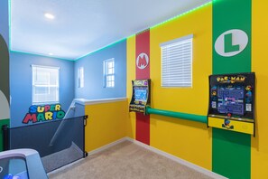 A room with a Super Mario theme, featuring a Pac-Man arcade machine and a Mario-themed poster.