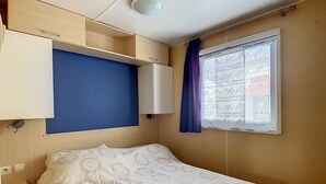 Ein Schlafzimmer mit einem Bett, einem Vorhangfenster, einer Deckenleuchte und einem fest installierten Regal über dem Bett.