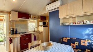 Eine kleine Küche mit Mikrowelle, Herd und Schränken. Ein Esstisch mit kariertem Tischläufer und ein Sofa mit gemusterten Kissen.