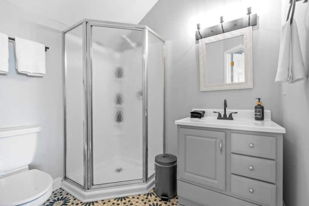 Une salle de bain avec une douche à parois de verre, des toilettes blanches, un meuble-lavabo avec un miroir et une poubelle.