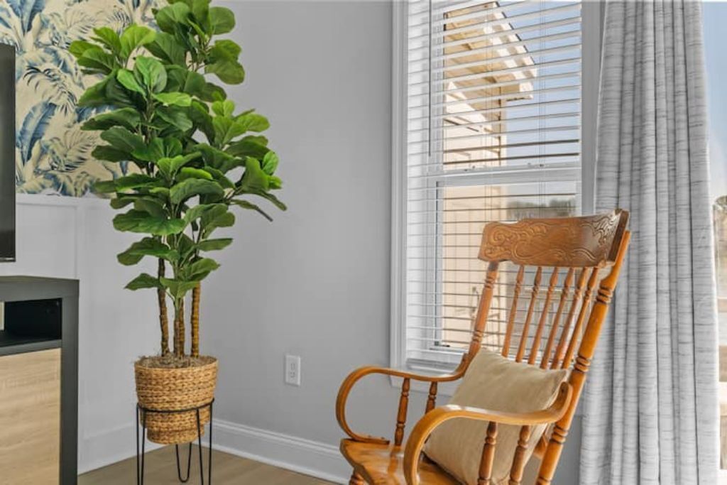 Une pièce avec une chaise en bois, une plante en pot et une fenêtre avec des stores.