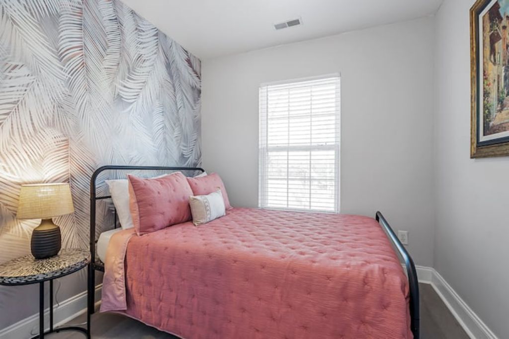Un dormitorio con cama, mesita de noche, lámpara, ventana y pared con diseño de hojas.