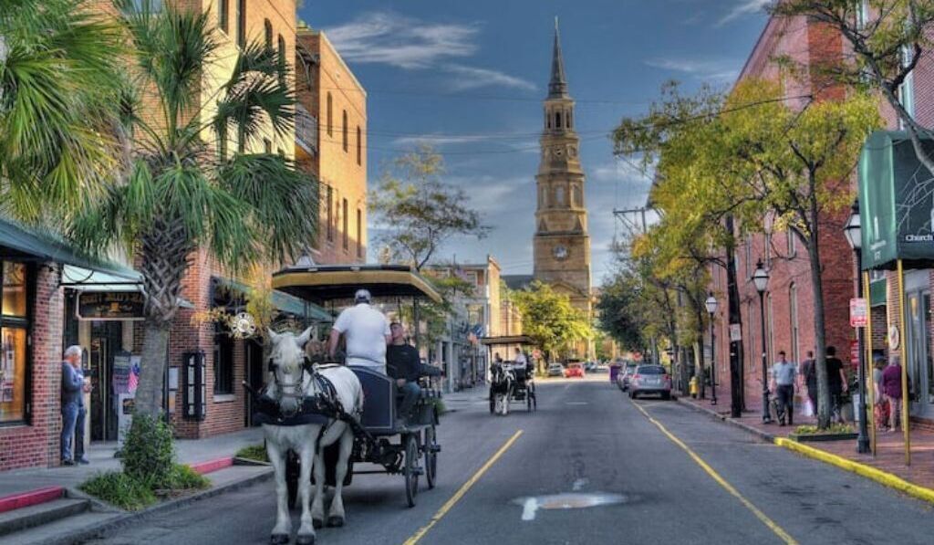 Una calle con un carruaje tirado por caballos, edificios y una torre destacada al fondo.