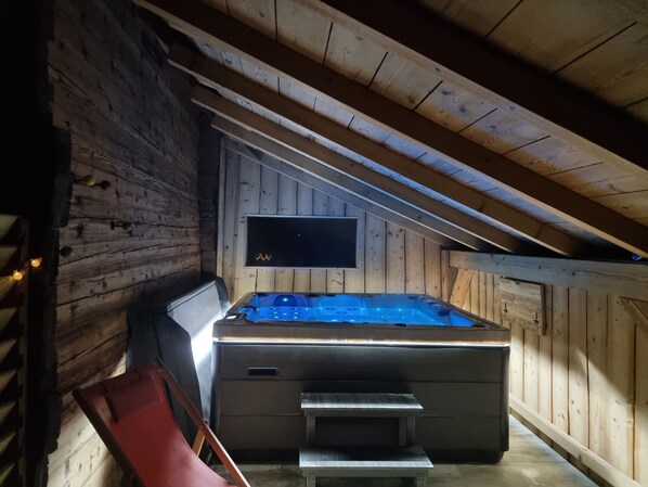 A hot tub in a wooden cabin with a TV mounted on the wall. - Atypical house for 2 with private jacuzzi (Saint-Pierre-de-Chartreuse)
