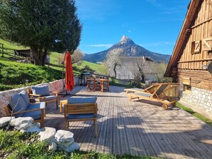 A wooden deck with outdoor seating, a stone wall, and a mountain view. - Atypical house for 2 with private jacuzzi (Saint-Pierre-de-Chartreuse)