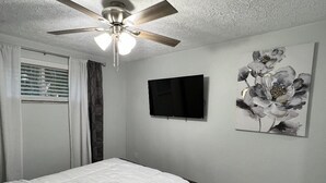 Ein Schlafzimmer mit einem Bett, einem Deckenventilator, einem Flachbildfernseher und einem an der Wand hängenden Kunstwerk.