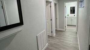 Ein Korridor mit weißer Decke, einem Lüftungsgitter und einer Tür zu einem Küchenbereich.