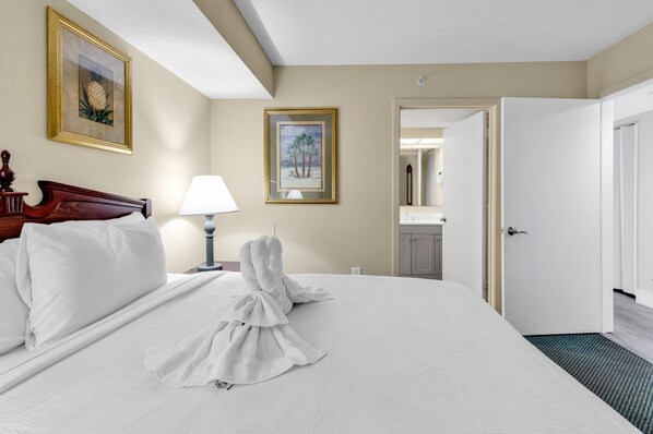 A hotel room with a neatly made bed, a wooden headboard, a lamp, and two framed pictures on the wall. - Atlantica Beachfront Getaway (Myrtle Beach)