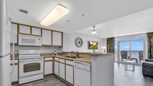 Una cocina moderna con electrodomésticos blancos, armarios de madera y un amplio ventanal con vistas al océano.