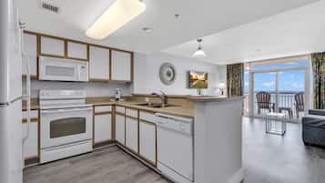A modern kitchen with white appliances, wooden cabinets, and a large window overlooking the ocean.