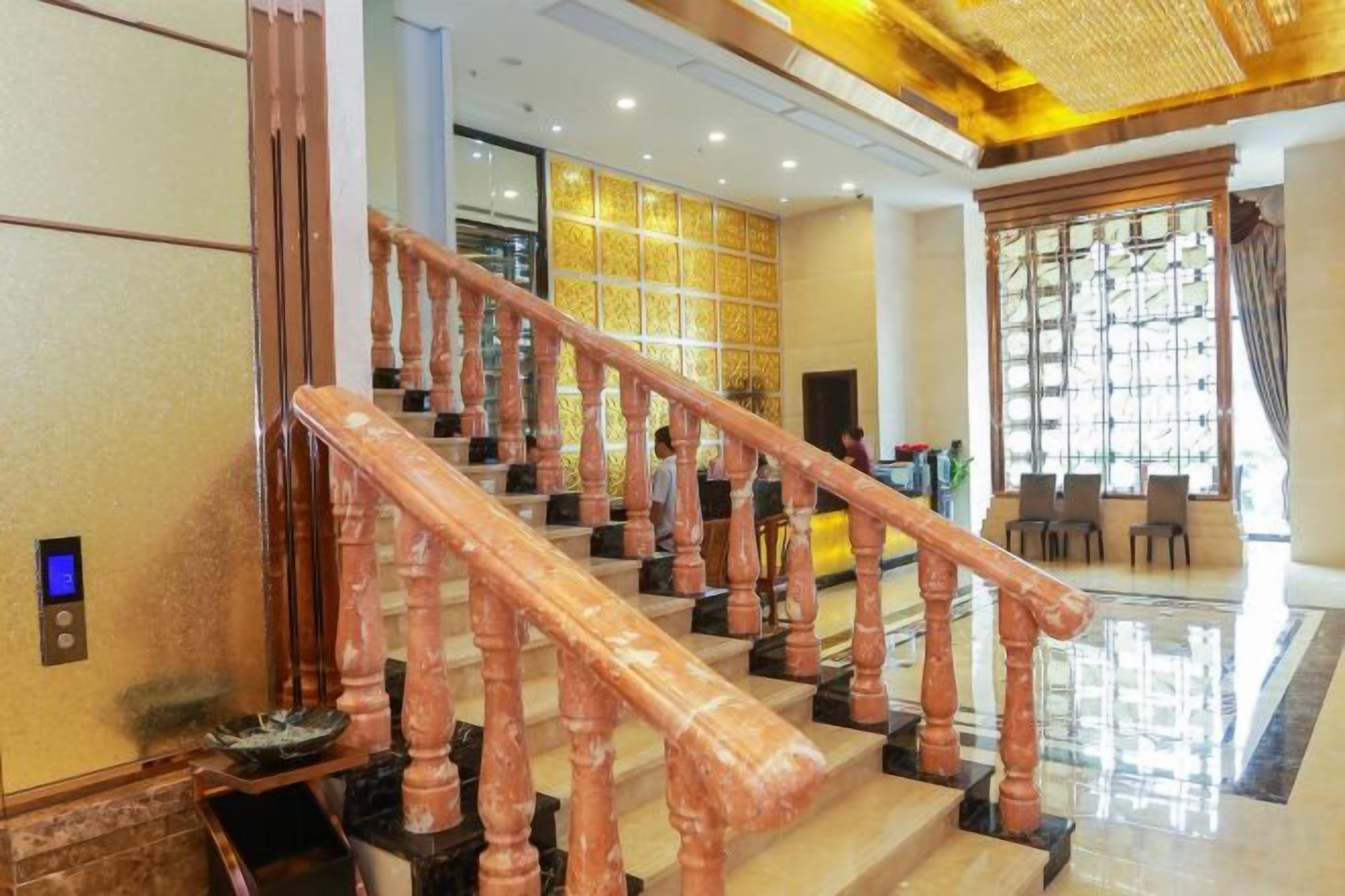 A staircase with wooden balusters leading to a lobby area with a seating arrangement and a large window with patterned curtains.