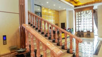 A staircase with wooden balusters leading to a lobby area with a seating arrangement and a large window with patterned curtains.