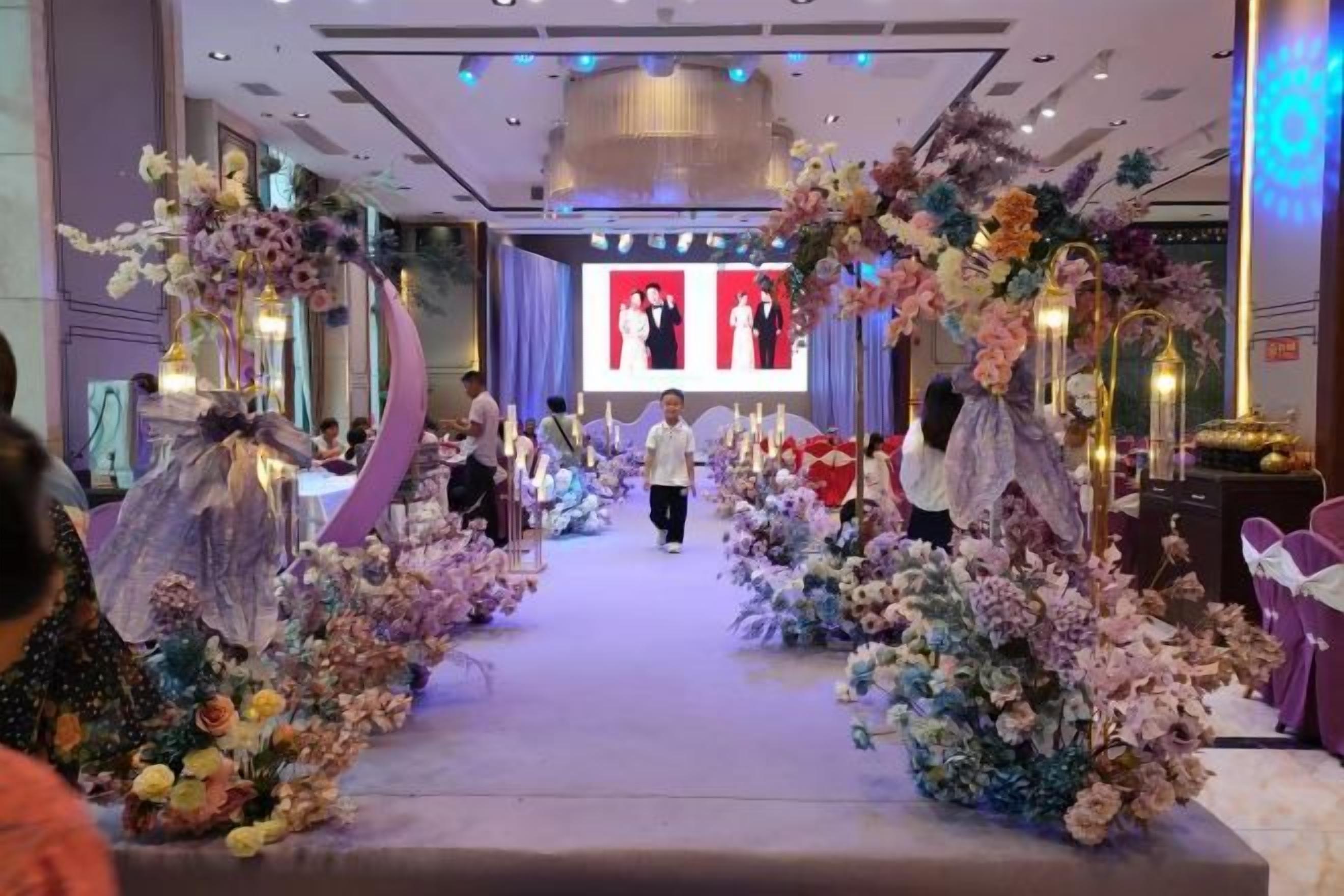 A decorated aisle with floral arrangements and a stage with a screen in the background.