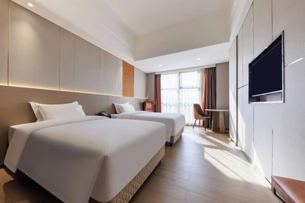 A hotel room with two beds, a desk, a chair, and a TV mounted on the wall.