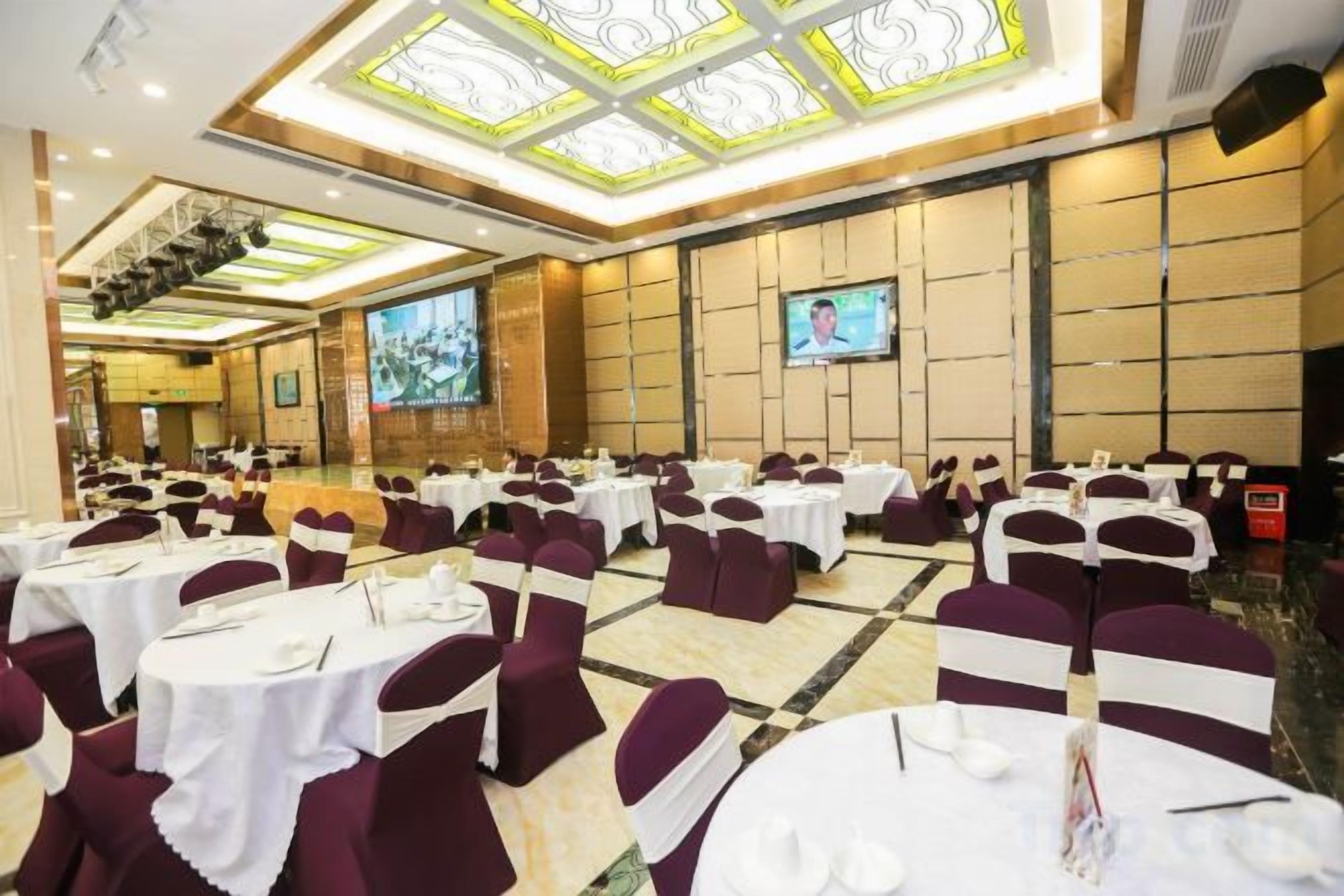 A banquet hall with round tables, chairs, and a large screen.