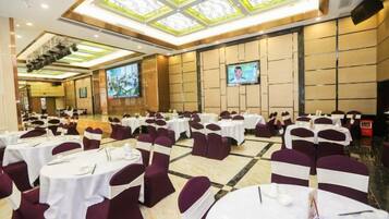 A banquet hall with round tables, chairs, and a large screen.
