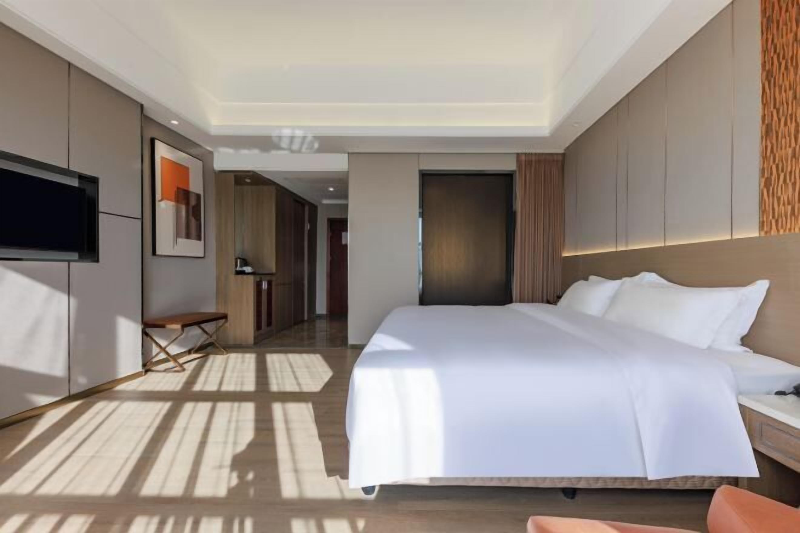 Ein modernes Hotelzimmer mit einem großen Bett, einem Flachbildfernseher, einer Bank und einem Schreibtisch.