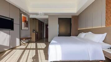 Ein modernes Hotelzimmer mit einem großen Bett, einem Flachbildfernseher, einer Bank und einem Schreibtisch.