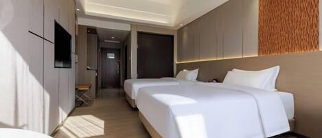 A modern hotel room with two beds, a flat-screen TV, and a wooden accent wall.