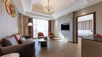 A modern hotel room with a sofa, armchairs, a coffee table, a TV, and a bed.