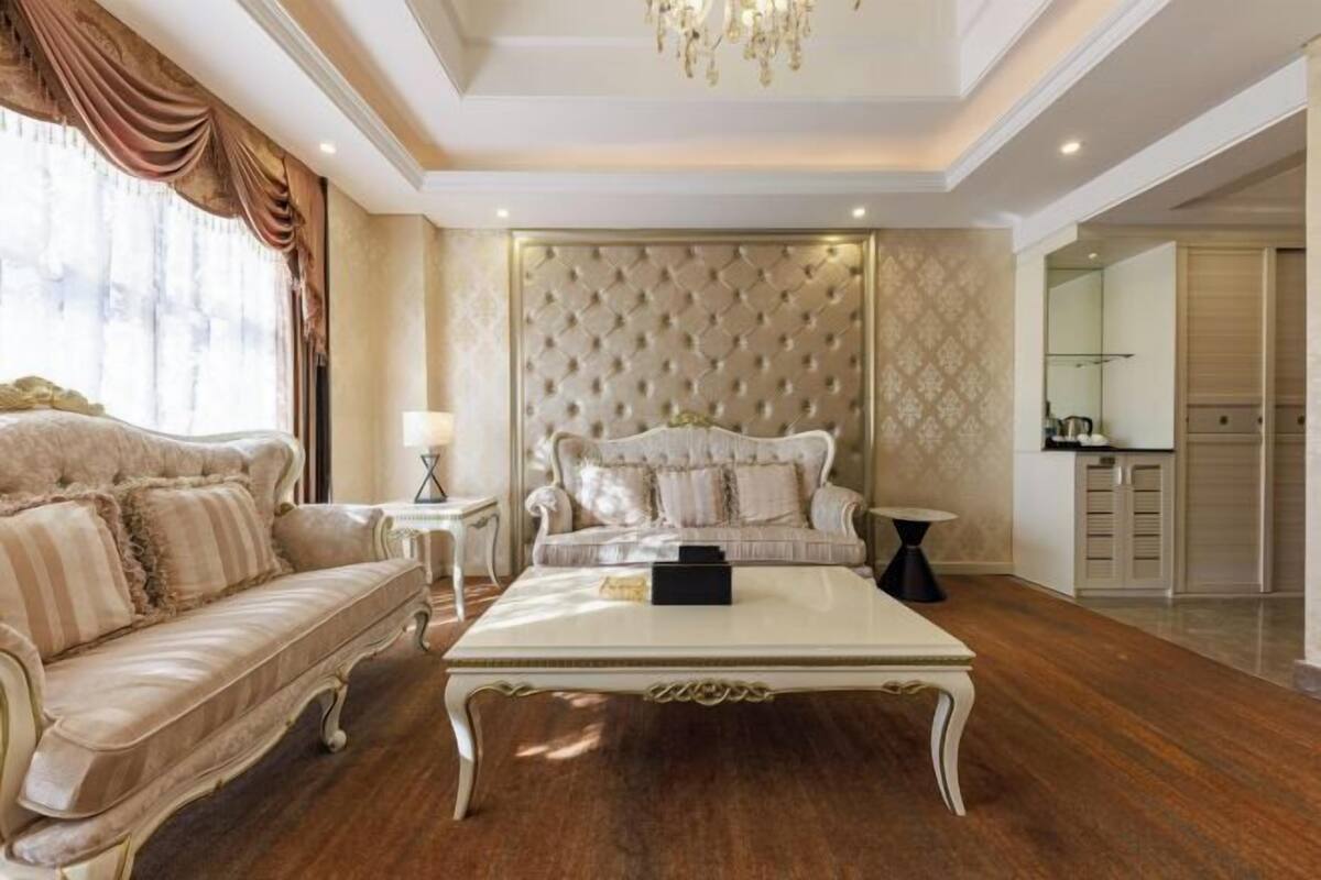 A luxurious living room with a tufted headboard sofa, a classic coffee table, and a chandelier.