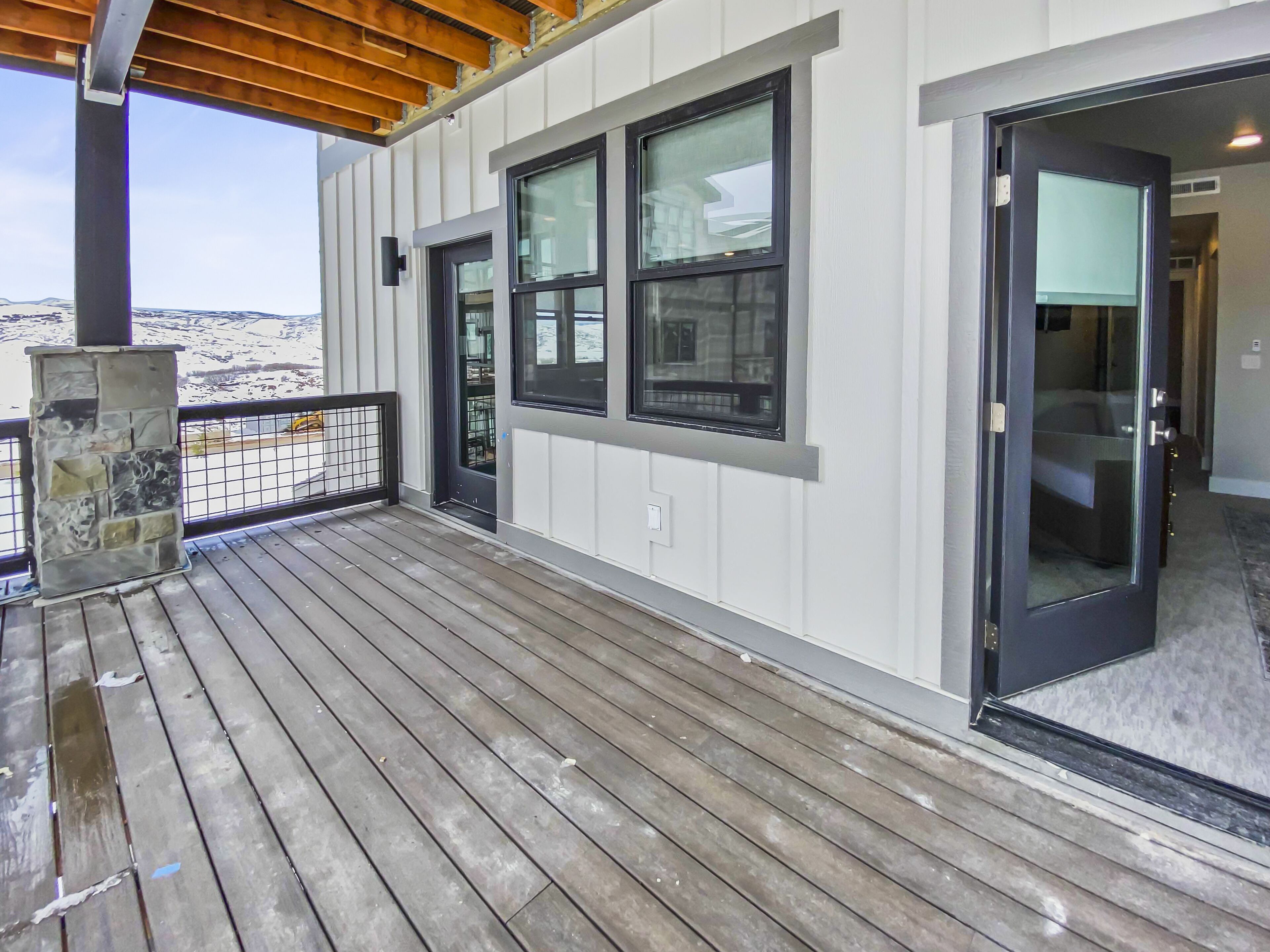 A wooden deck with a stone fireplace, a sliding glass door, and a view of a snowy landscape.