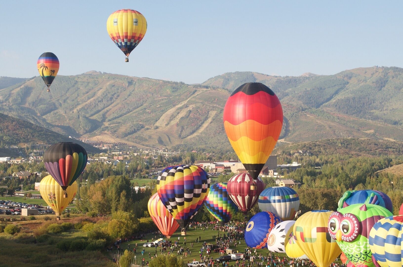 Colorful hot air balloons drift over mountains and valleys, creating a spectacular display during the annual balloon festival in this scenic area.