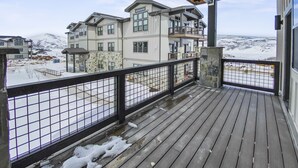 A wooden deck with a metal railing overlooking a snowy landscape and buildings.