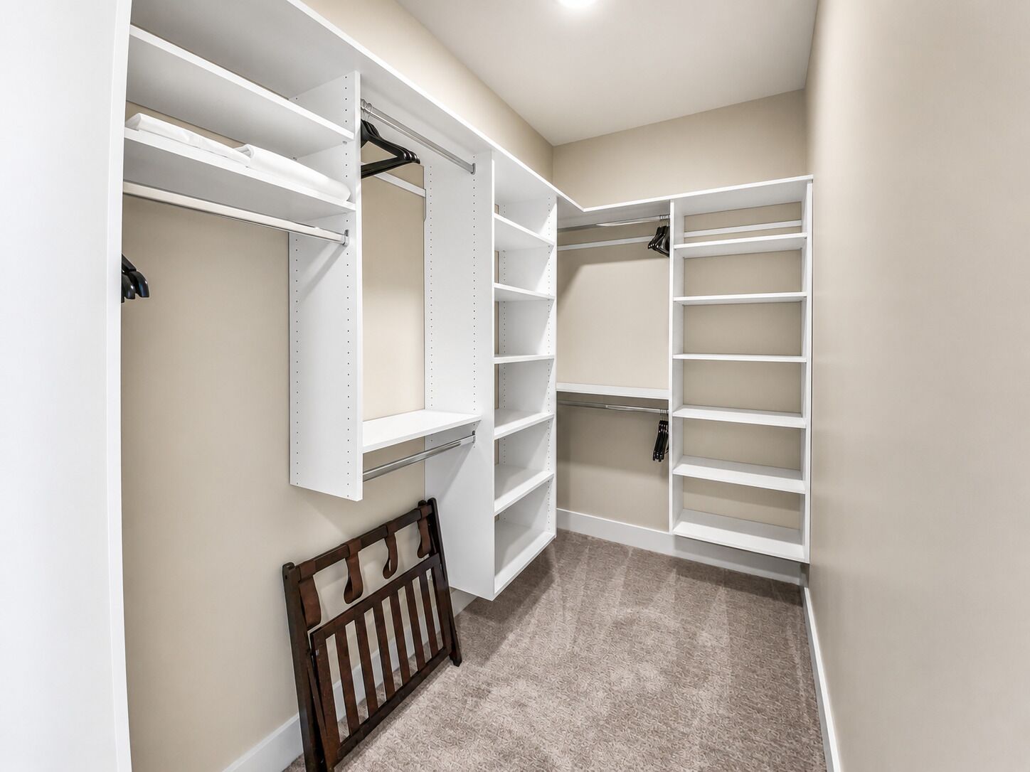 A walk-in closet with white shelving, a wooden bench, and a hanging shoe rack.