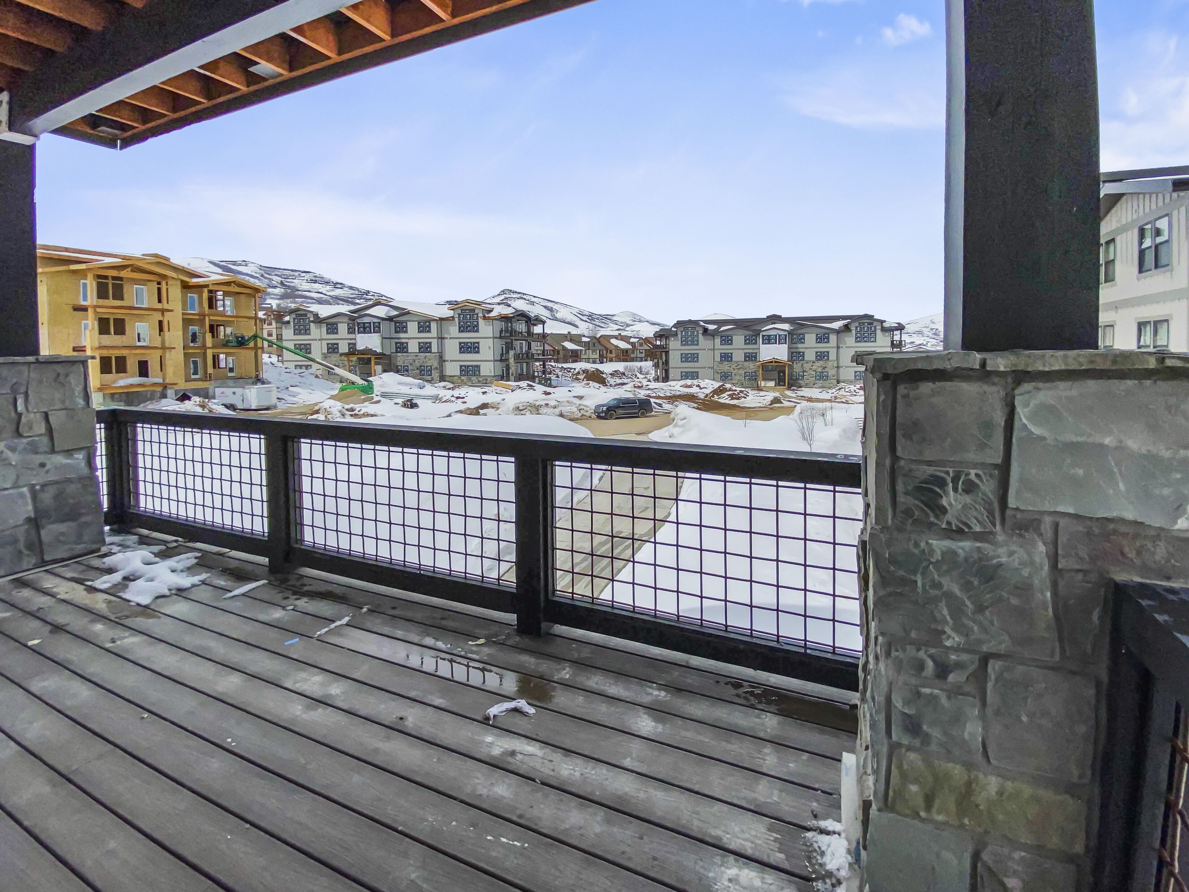A wooden deck with a stone wall and metal railing overlooking a snowy landscape with buildings.
