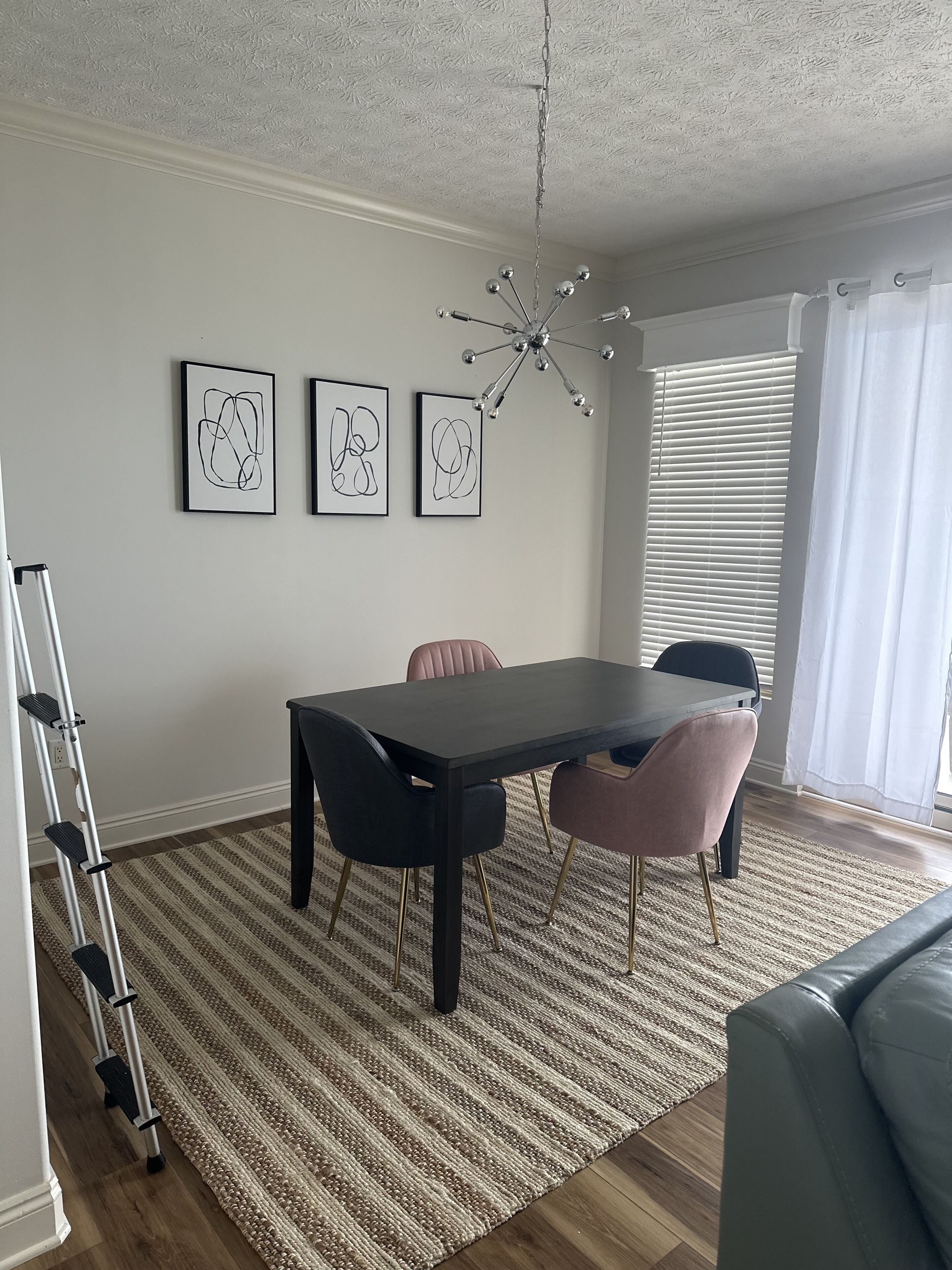 A dining area with a table, chairs, a chandelier, and artwork on the wall.