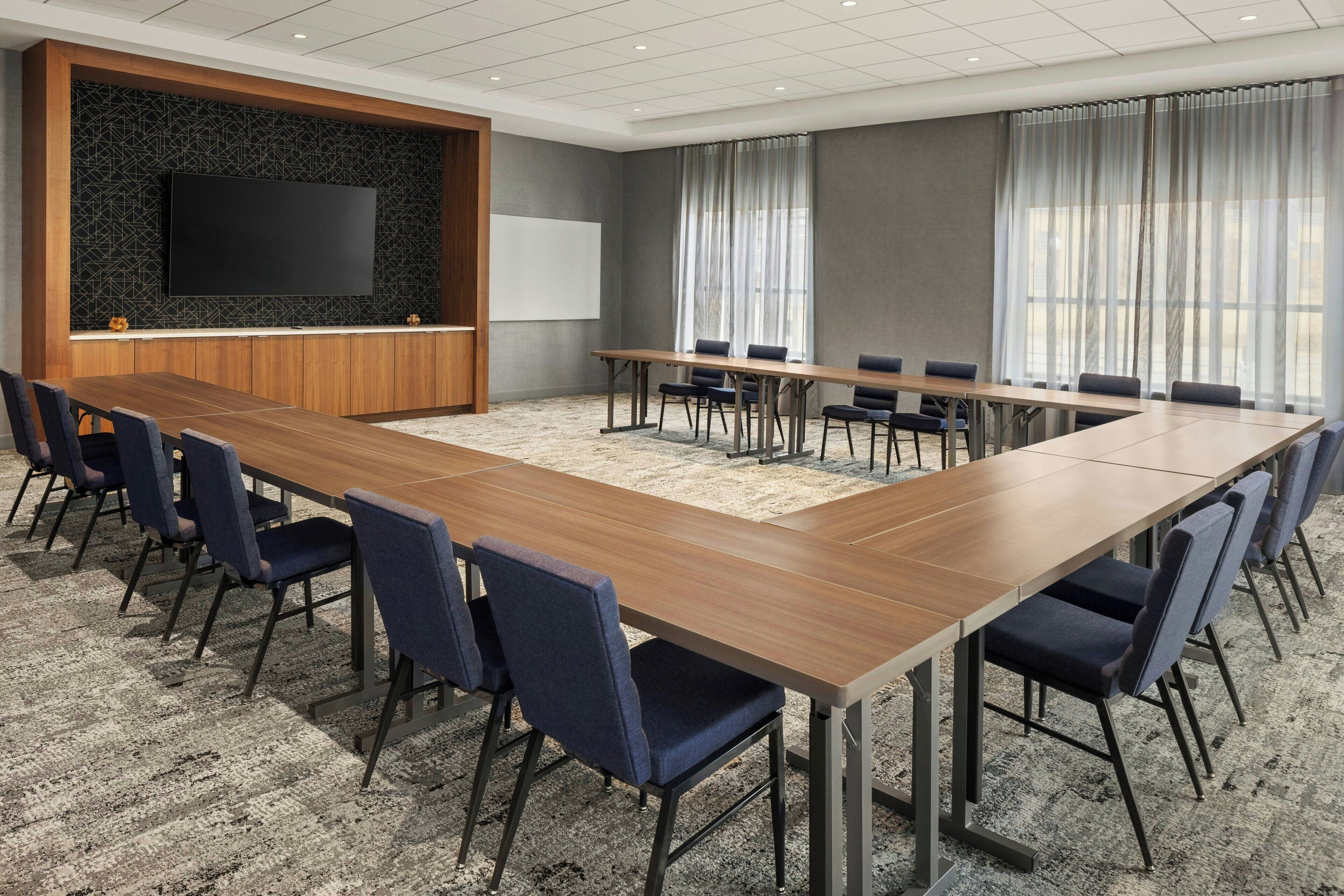 A conference room with a long table, chairs, a TV, and a whiteboard.