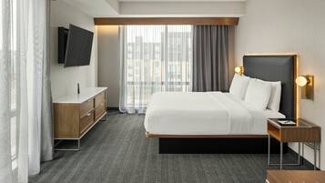 A modern hotel room with a large bed, a flat-screen TV mounted on the wall, a wooden nightstand, and a desk with a chair.