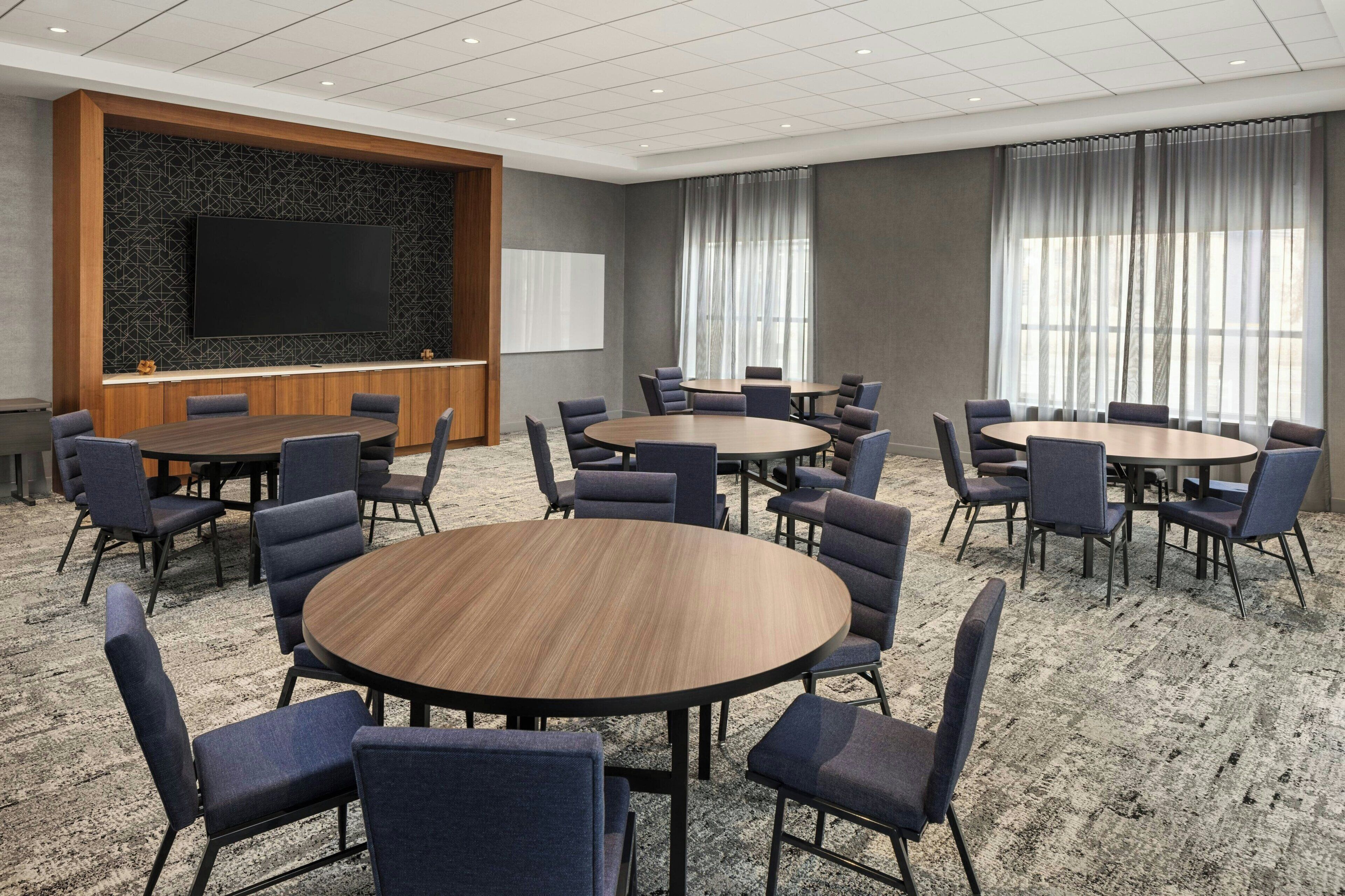 Une salle de conférence équipée de plusieurs tables et chaises, d’un grand téléviseur à écran plat et d’un tableau blanc.