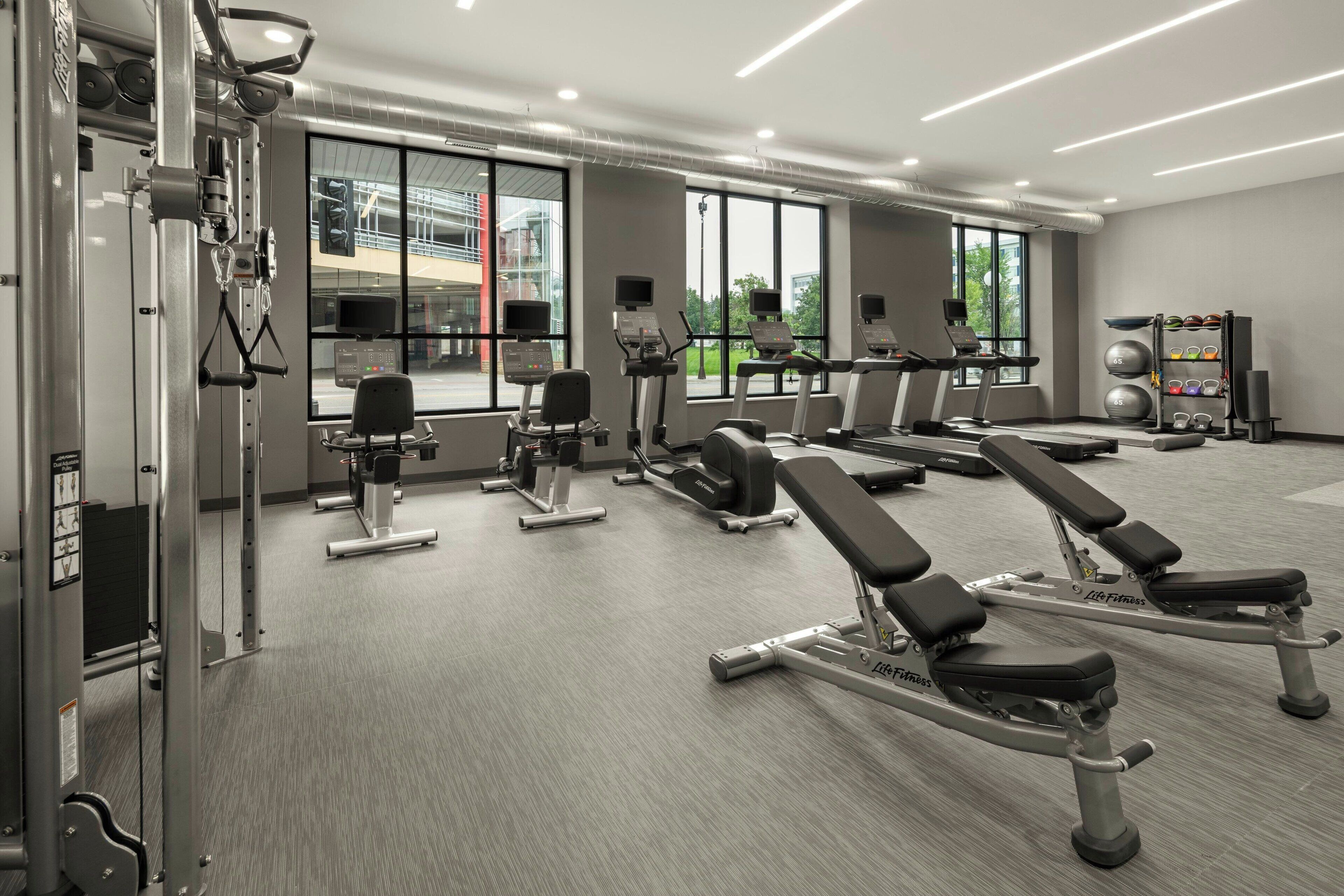 A modern gym with various exercise equipment, large windows, and a clean, well-lit interior.