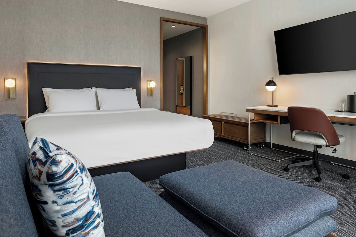 Une chambre d’hôtel avec un grand lit, un bureau, une chaise et un téléviseur à écran plat.