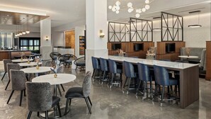 Een moderne hotel lobby met ronde tafels, een bar en een groot televisiescherm.