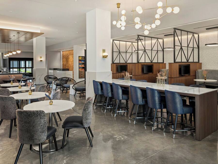 Eine moderne Hotelhalle mit runden Tischen, einer Bar und einem großen Fernseher.
