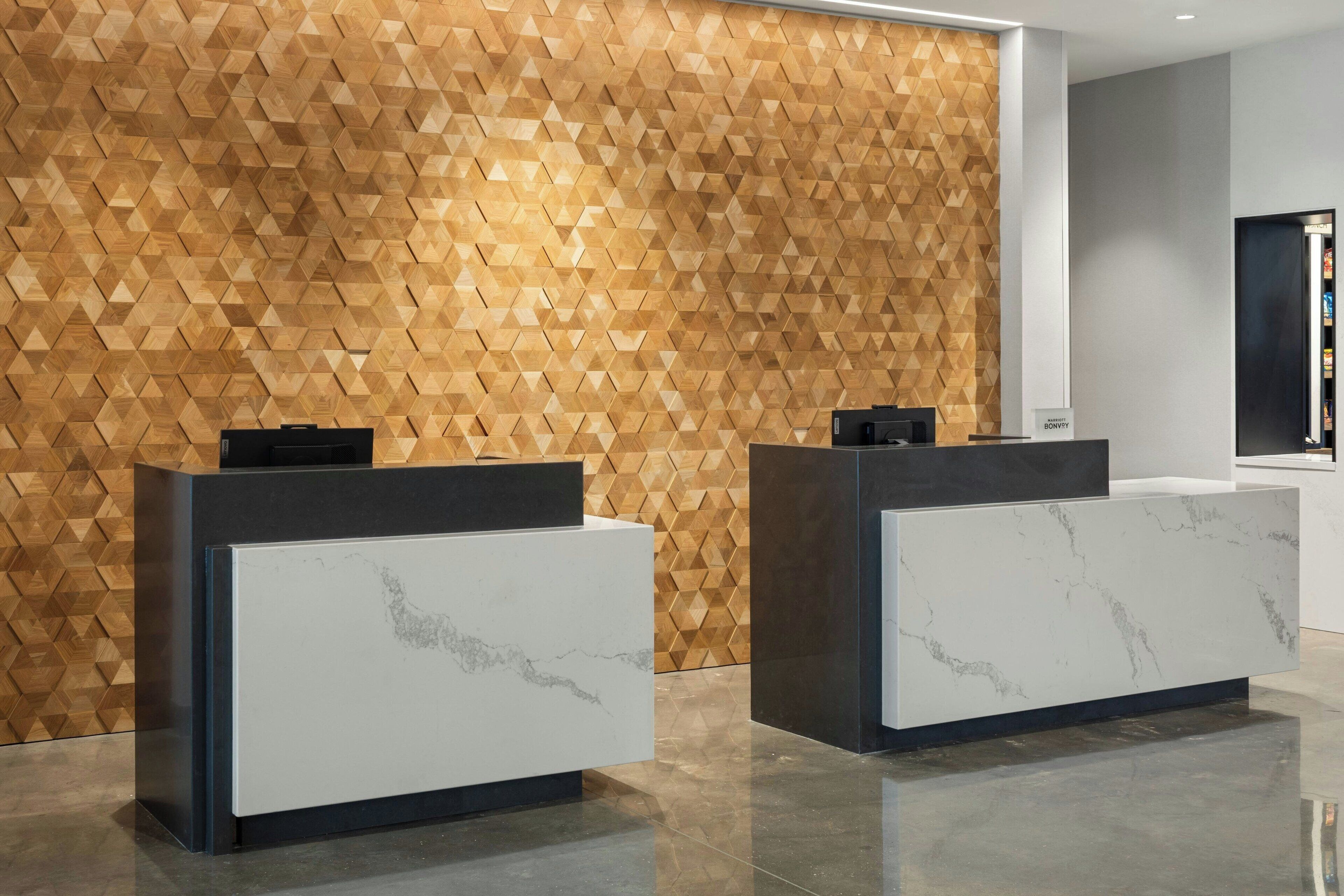 A reception area with two reception desks, one white and one dark, in front of a geometric patterned wall.
