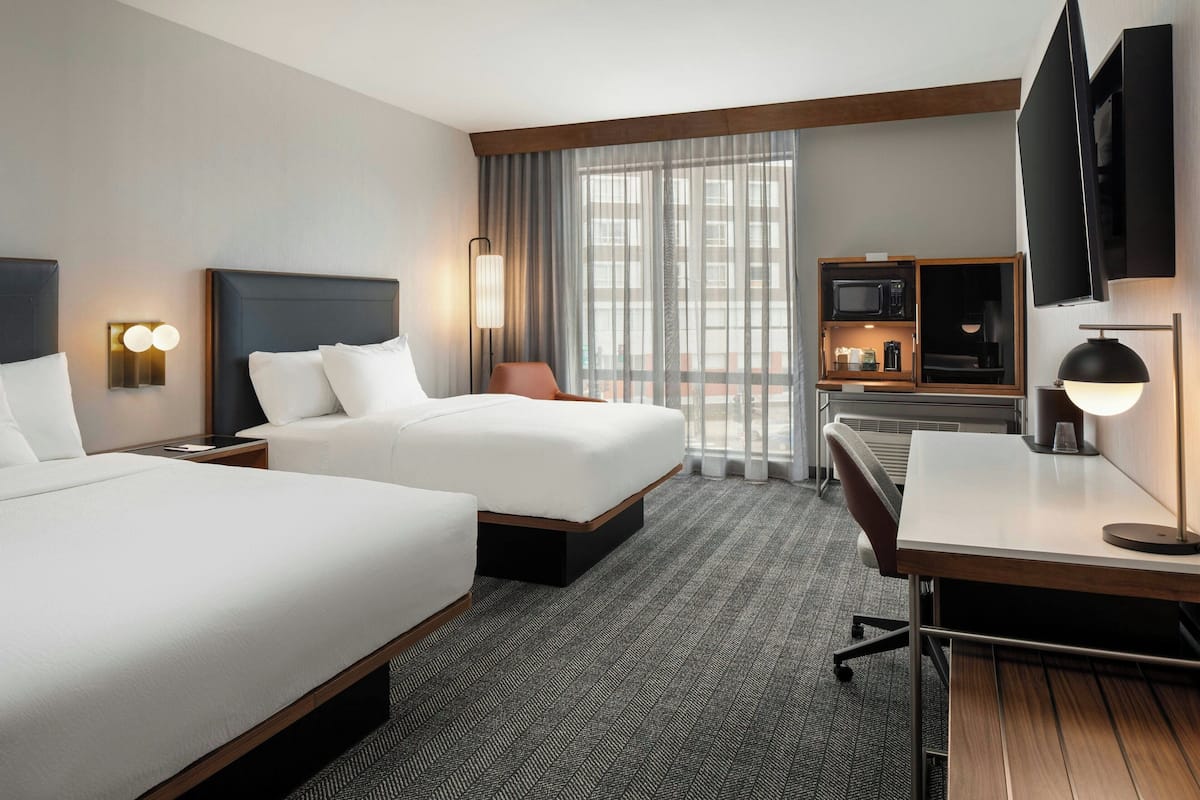 Une chambre d’hôtel avec deux lits, un bureau, une chaise, une télévision et un mini-bar.